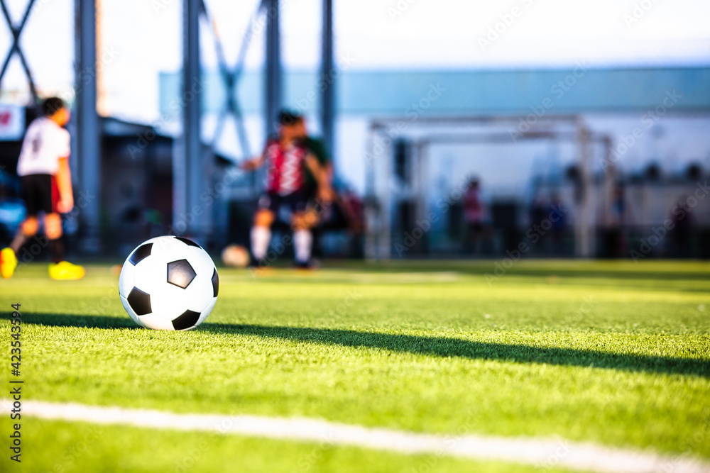 Soccer ball on green artificial turf with blurry coach and soccer team are training. Blurry kid soccer players training in soccer academy. Soccer ball on green artificial turf with blurry coach and soccer team are training. Blurry kid soccer players training in soccer academy.