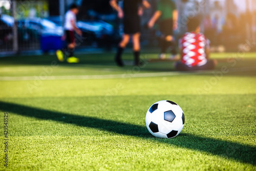 Soccer ball on green artificial turf with blurry coach and soccer team are training. Blurry kid soccer players training in soccer academy.