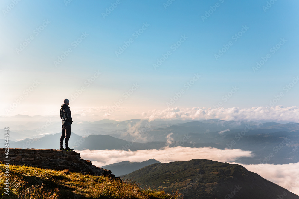 man standing at the edge of the cliff looking at mountains