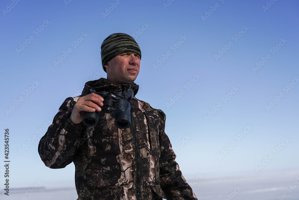 a man in military clothes holds binoculars in his hand and looks. In the background snowy steppe and blue sky. a man in military clothes holds binoculars in his hand and looks. In the background snowy steppe and blue sky.