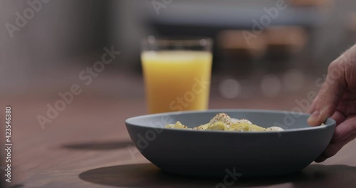 Slow motion man put blue boawl with pesto fettuccine on walnut table with orange juice photo