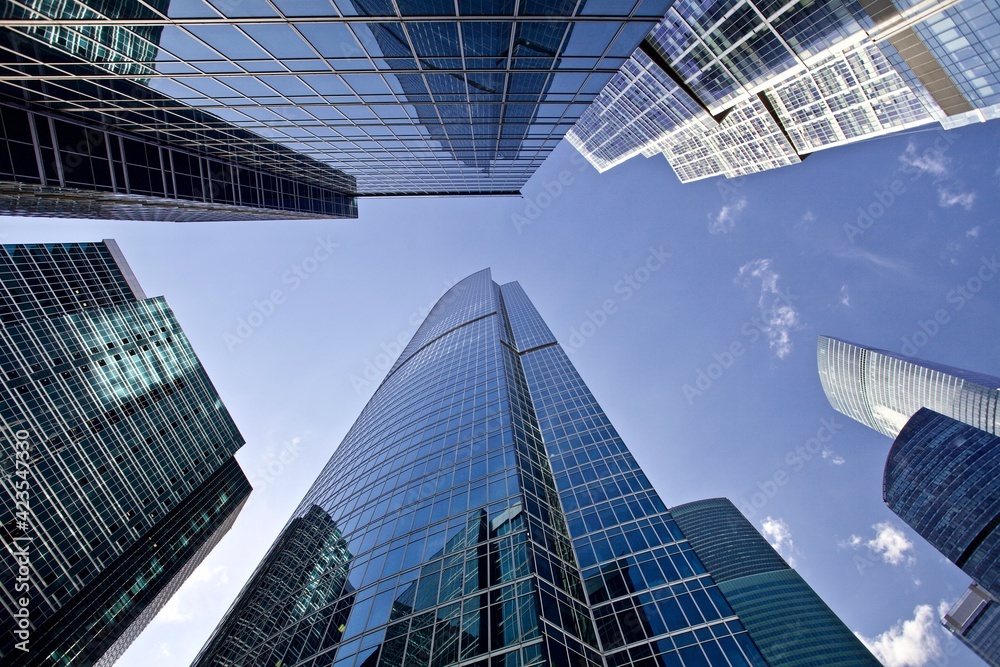 Fototapeta premium Bottom up view of modern office buildings in the city's business district. Glass facades of skyscrapers with contrasting highlights and reflections. Economy development, finance and business concept. 