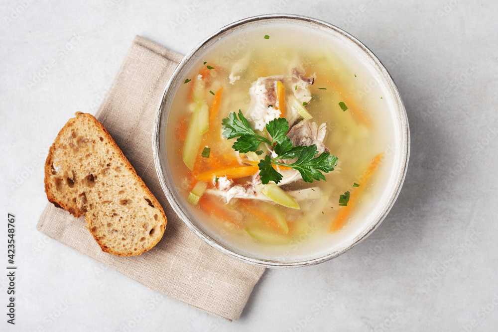 chicken soup in a bowl on a gray table with a piece of bread, top view, close-up chicken soup in a bowl on a gray table with a piece of bread, top view, close-up