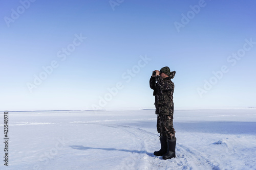 a man in a military uniform looks through binoculars against a background of blue sky and winter landscape