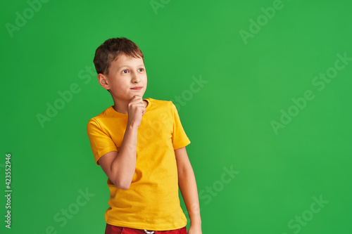 Tapet pensive 8-year-old boy in a yellow T-shirt stands and thinks on a green background