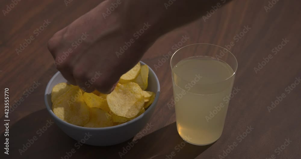 Slow motion man hand pick potato chips from blue bowl with ginger beer on background
