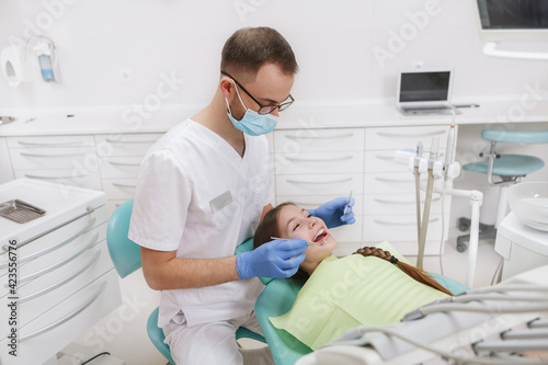 Male dentist working at his clinic, examining teeth of young girl