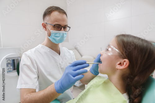 Professional dentist wearing medical mask, examining teeth of young patient