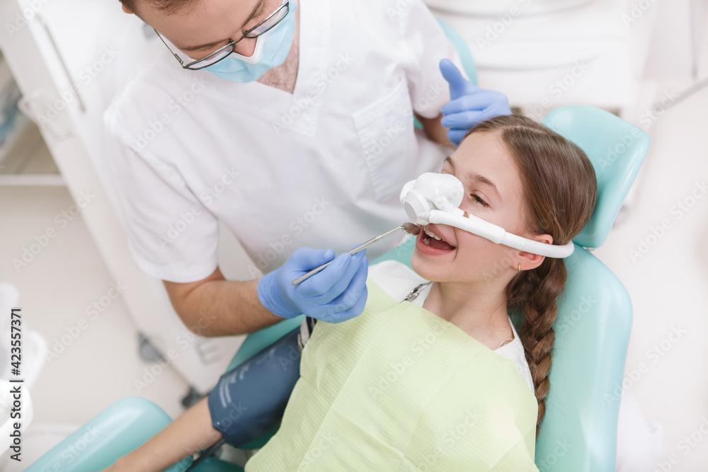 Young girl having her teeth treated while having inhalation sedation mask on