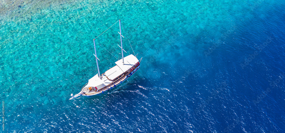 Sailing yacht in Maldives islands. Aerial drone view of white sailboat anchored, crystal clear turquoise ocean. Summer recreational sport activity, snorkeling, diving. Amazing aerial sea nature banner