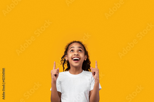 Excited black girl pointing up at free copy space