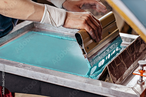 selective focus photo of male hands with squeegee. serigraphy production. printing images on t-shirts by silkscreen method in a design studio photo
