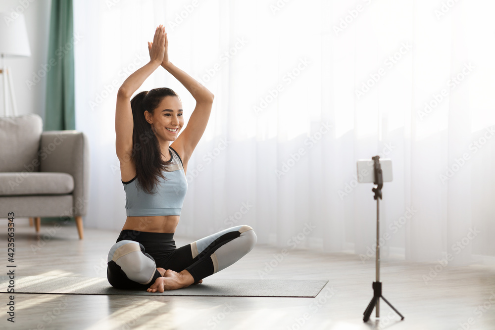 Good looking young lady watching online yoga class, using smartpohne