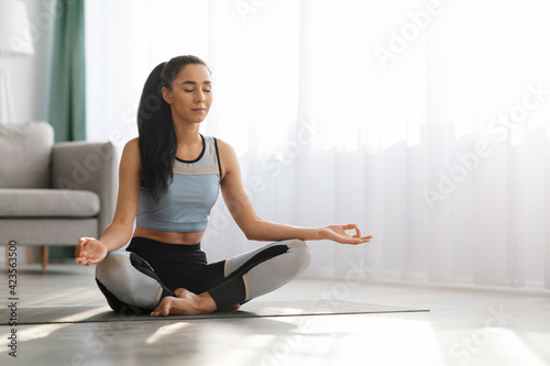 Young woman in sportswear meditating at home