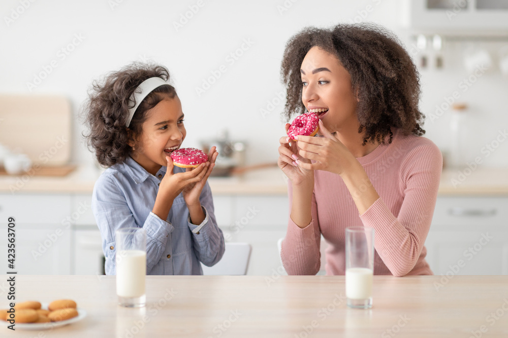 Black mother and daughter eating sweet food in kitchen Black mother and daughter eating sweet food in kitchen