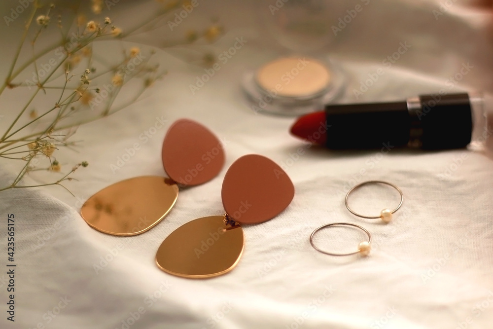 Various make up products, earrings, rings and flowers on white background. Selective focus. Various make up products, earrings, rings and flowers on white background. Selective focus.
