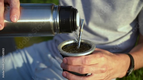 Man Pouring Hot Water Into Yerba Mate Drink From Vacuum Flask. - close up photo