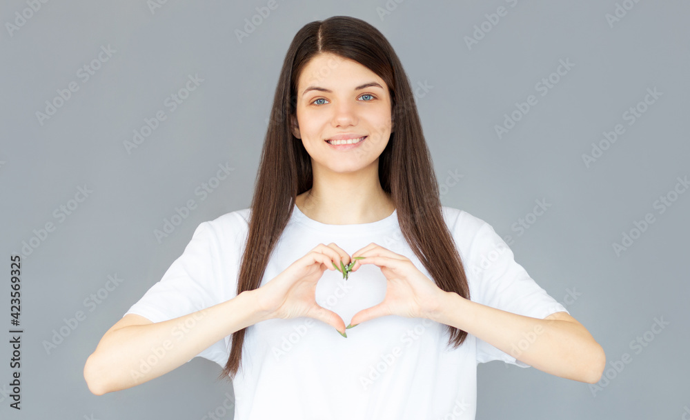 Portrait of a smiling young woman showing heart gesture with two hands and looking at camera isolated over gray background Portrait of a smiling young woman showing heart gesture with two hands and looking at camera isolated over gray background