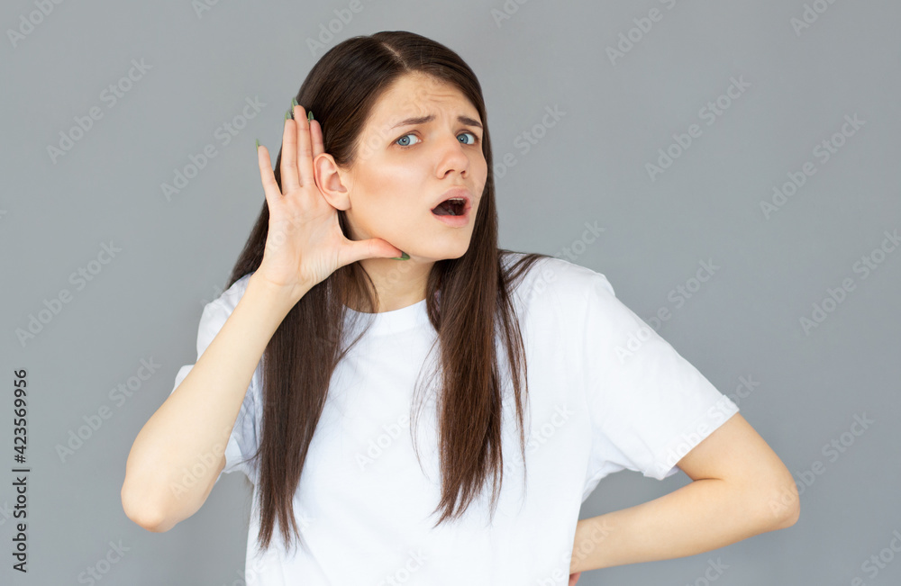 Tell me louder. Portrait of attentive brunette young woman with hairstyle in casual style standing with hand gesture on ear and looking at camera. studio shot isolated on gray background. Tell me louder. Portrait of attentive brunette young woman with hairstyle in casual style standing with hand gesture on ear and looking at camera. studio shot isolated on gray background.