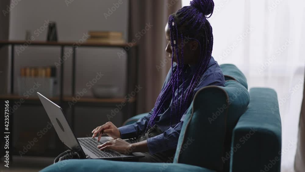 afro-american female student is learning online at home, lady is using laptop, typing text on keyboard