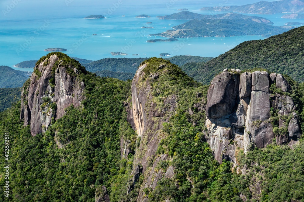 Fototapeta premium Close up view and detail of the three rock formation peaks covered with Serra do Mar green vegetation with Carioca bay coastline at far background.