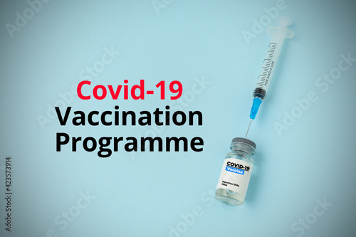 COVID-19 VACCINATION PROGRAMME text with a bottle of vaccine and syringe on blue background. Covid-19 or Coronavirus Concept.