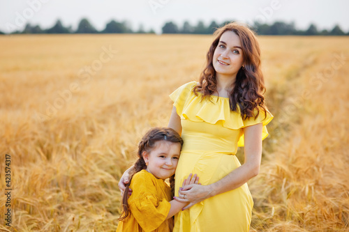 Pregnant mother and daughter in a wheat field at sunset. Gentle family hugs of mother and child in nature.