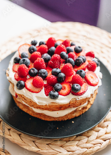 Meringue cake with fresh forest berries and cream on black plate