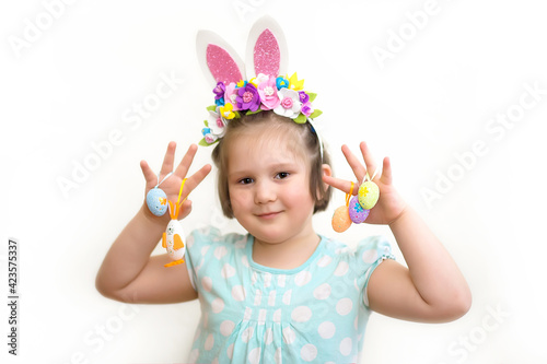 Little girl in a hoop with Easter bunny ears and flowers holds decorative Easter eggs and a bunny on a white background.Happy Easter  banner  postcard  copy space. Selective focus 