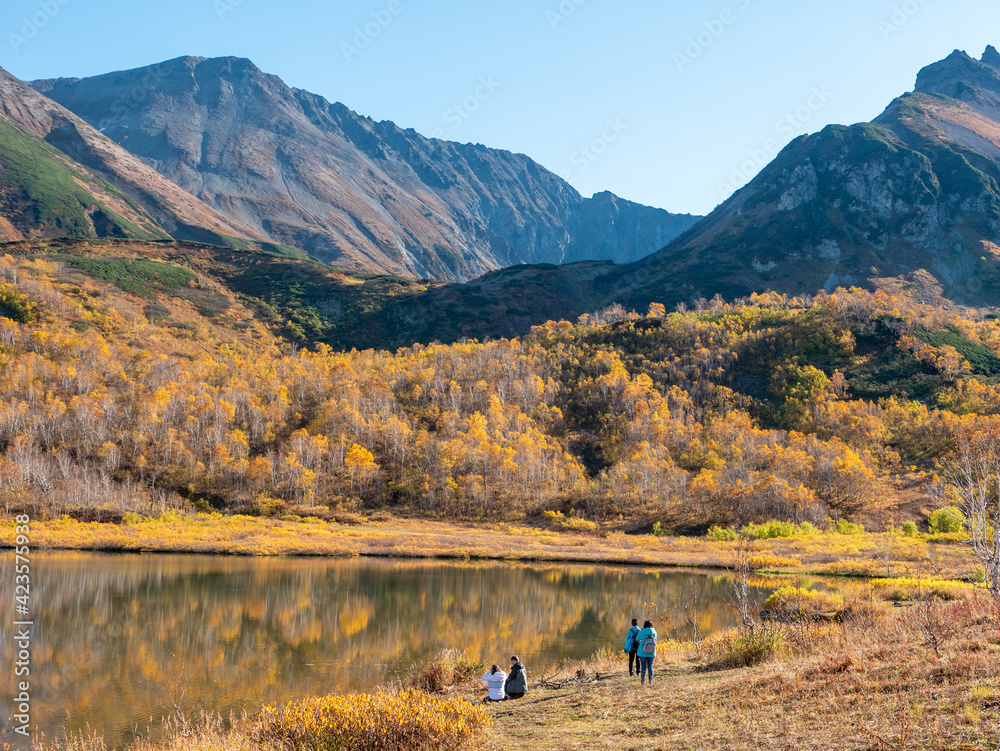 Nice view of the lake and the Vachkazhets mountain range. High mountains against the background of an autumn forest with yellow leaves and the smooth surface of the lake. Kamchatka Peninsula, Russia.