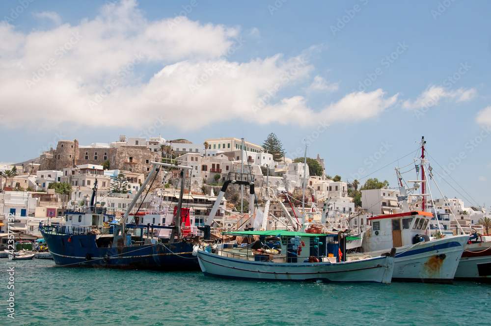 Fishing boats anchored in the old harbor of Naxos Island in Greece. In the background the castle, the city, and the partially cloudy sky.
