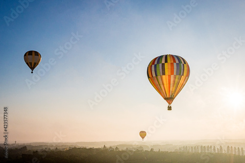 Bunte Heißluftballons fliegen kurz nach Sonnenaufgang über eine märchenhafte Landschaft mit Bäumen