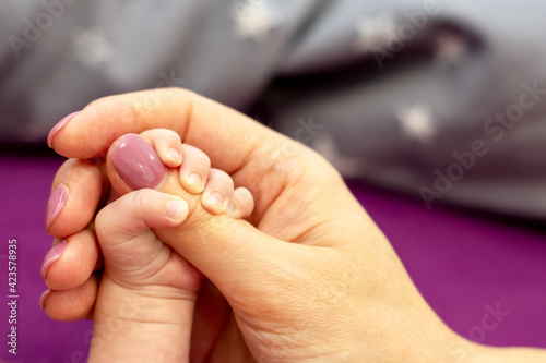 Ein Baby hält sich am Daumen der Mutter mit seinen Fingern fest