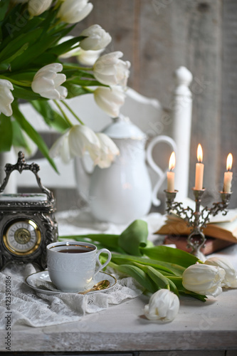 A bouquet witte tulips in a vase, a white alarm clock en kopje koffie op witte tafel. traditional English tea, high tea 