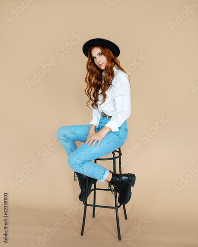redhead girl in black hat sitting on peach color background