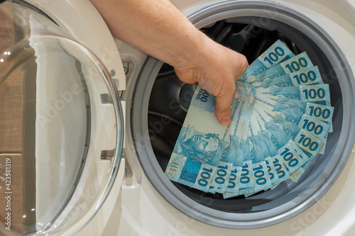 Brazilian money, the concept of money laundering from illegal activities. The man puts a large amount of banknotes into the washing machine