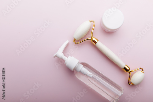Face and body care concept. Stone roller with cream and oil for massage on pink background