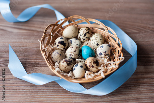 easter eggs in a wicker basket with a blue ribbon on a wooden background
