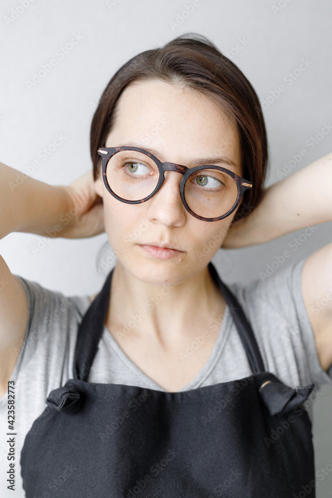 portrait of a young and beautiful Caucasian woman with dark hair and glasses, who pulls her hair back. the girl does her hair and looks thoughtfully away portrait of a young and beautiful Caucasian woman with dark hair and glasses, who pulls her hair back. the girl does her hair and looks thoughtfully away