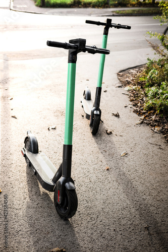 Electric scooters standing on the street in the park zone. E-scooter or kick scooter using with mobile app. Modern, ecological, eco-friendly urban transport. Summer in the city. Copy space, close up