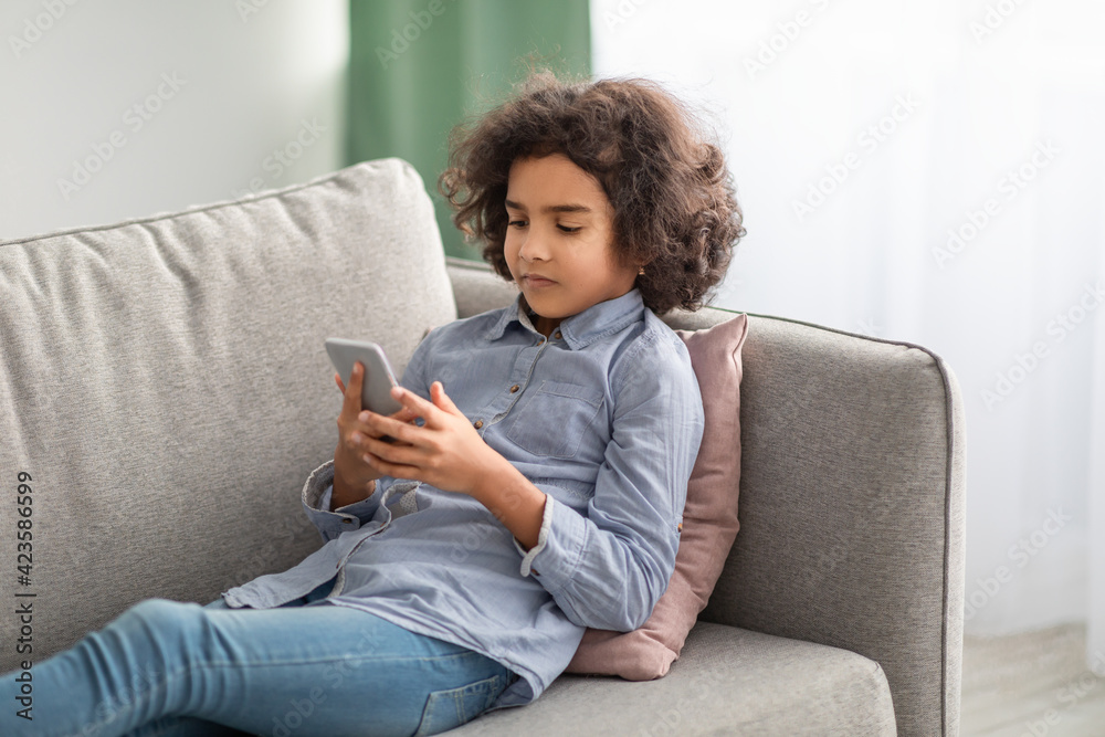 Black girl using her smartphone resting on sofa Black girl using her smartphone resting on sofa