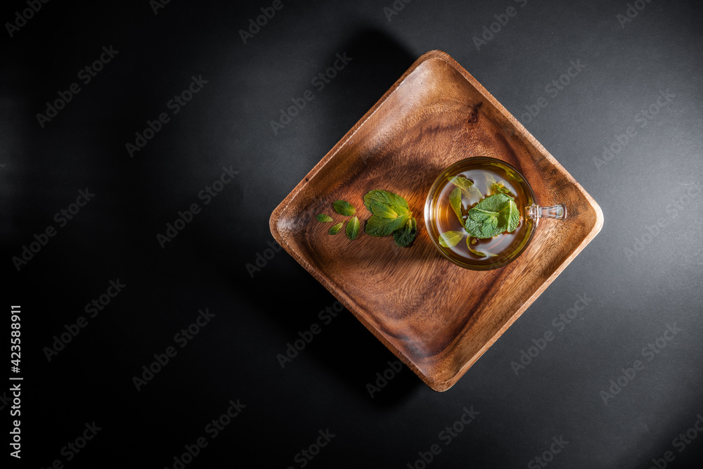 Mint tea leaves in a cup on wooden saucer, isolated on gray black background Mint tea leaves in a cup on wooden saucer, isolated on gray black background