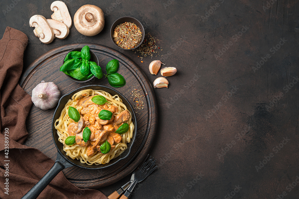 Culinary background with pasta and creamy mushroom sauce, basil, garlic and spices on a dark brown background.