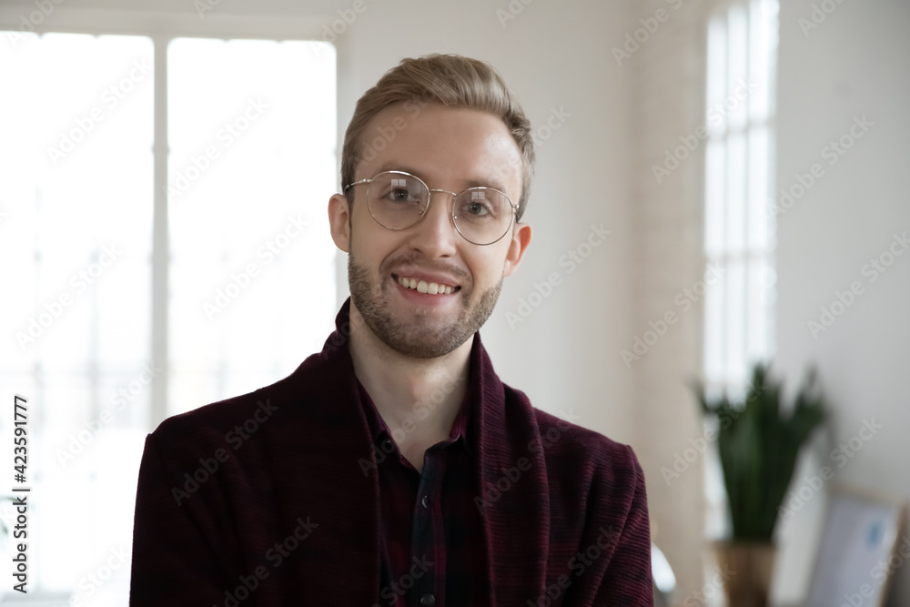 Headshot portrait of young Caucasian 20s male employee in glasses posing in office. Profile picture of smiling millennial businessman or CEO show leadership at workplace. Recruitment concept. Headshot portrait of young Caucasian 20s male employee in glasses posing in office. Profile picture of smiling millennial businessman or CEO show leadership at workplace. Recruitment concept.