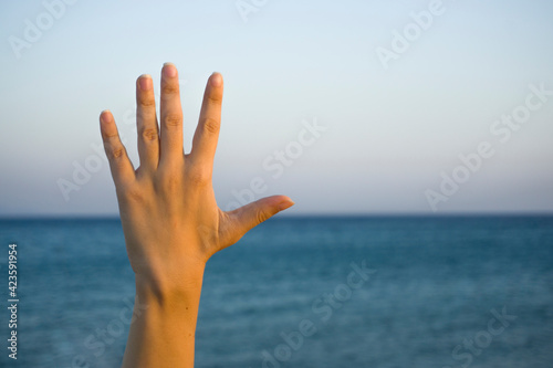 Woman hand doing showing number five gesture symbol on blue summer sky nature background. Gesturing number 5. Number five in sign language. Fifth, counting down five concept. Five fingers up. 