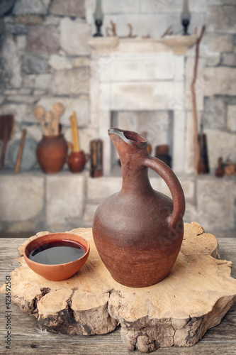 A traditional Georgian wine jug and clay cup on the wooden table in marani (cellar for storing wine in special pitchers) photo