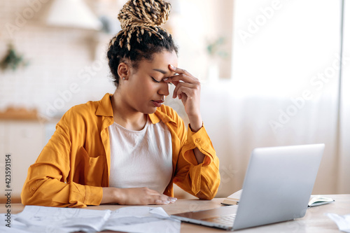 Overworked frustrated young african american student girl or freelancer, in casual clothes, studying or working at home uses laptop, thinking about a problem taking break experiencing stress need rest