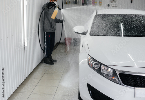Modern washing with foam and high-pressure water of a white car. Car wash