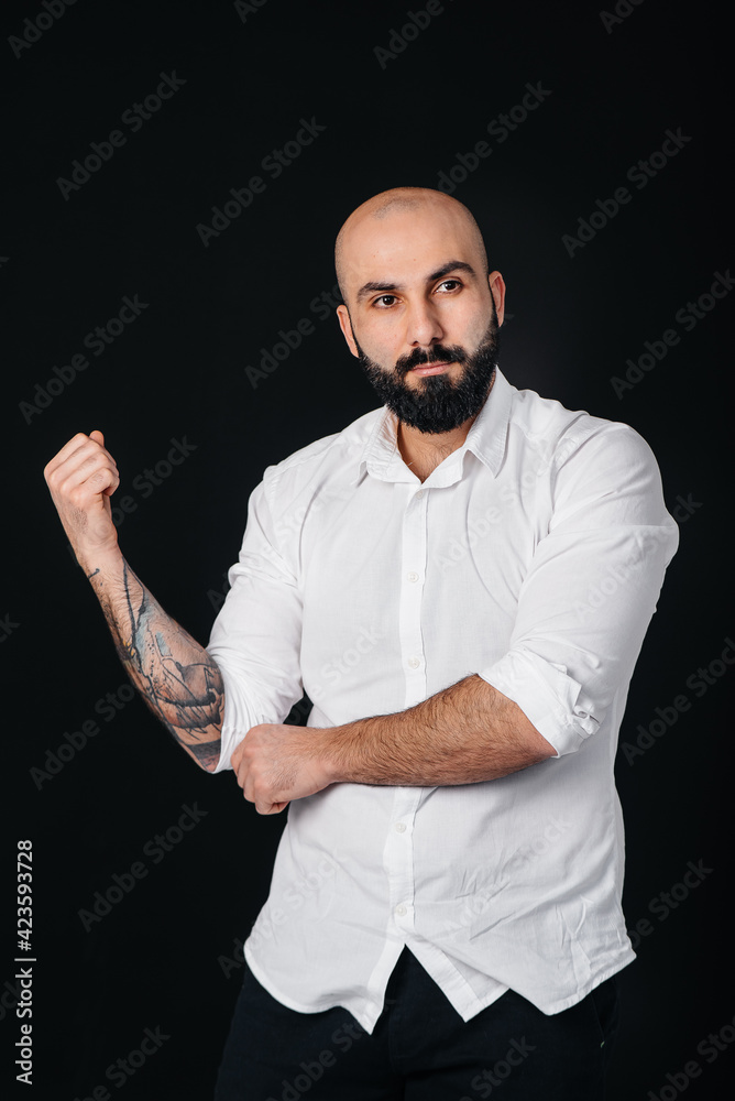 A young bearded man in a white shirt and tattoos stands on a black background.
