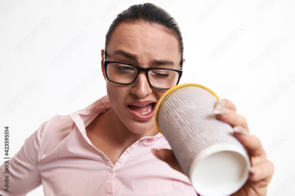 Confused woman in eyeglasses looking through takeaway paper cup, expressing surprise and dissatisfaction . Close Up, white background, copy space Confused woman in eyeglasses looking through takeaway paper cup, expressing surprise and dissatisfaction . Close Up, white background, copy space